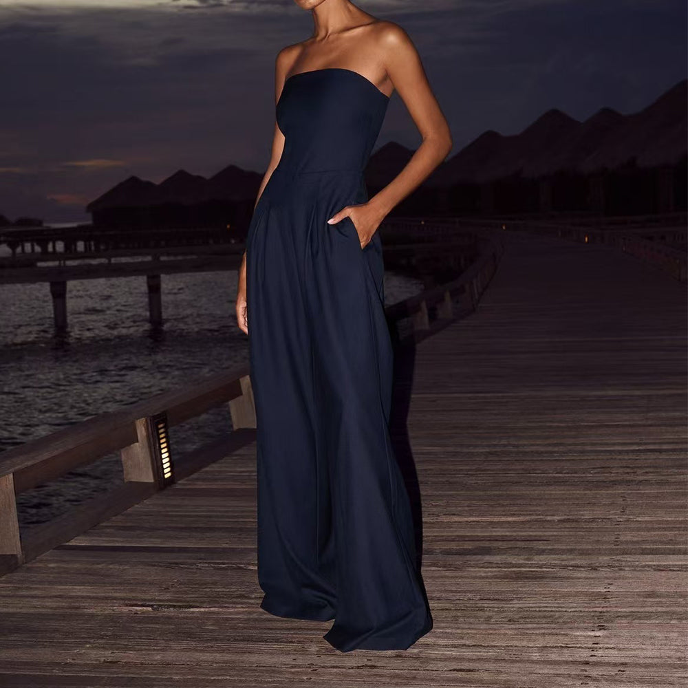 Woman in a dark blue strapless gown standing on a wooden dock by water at dusk.