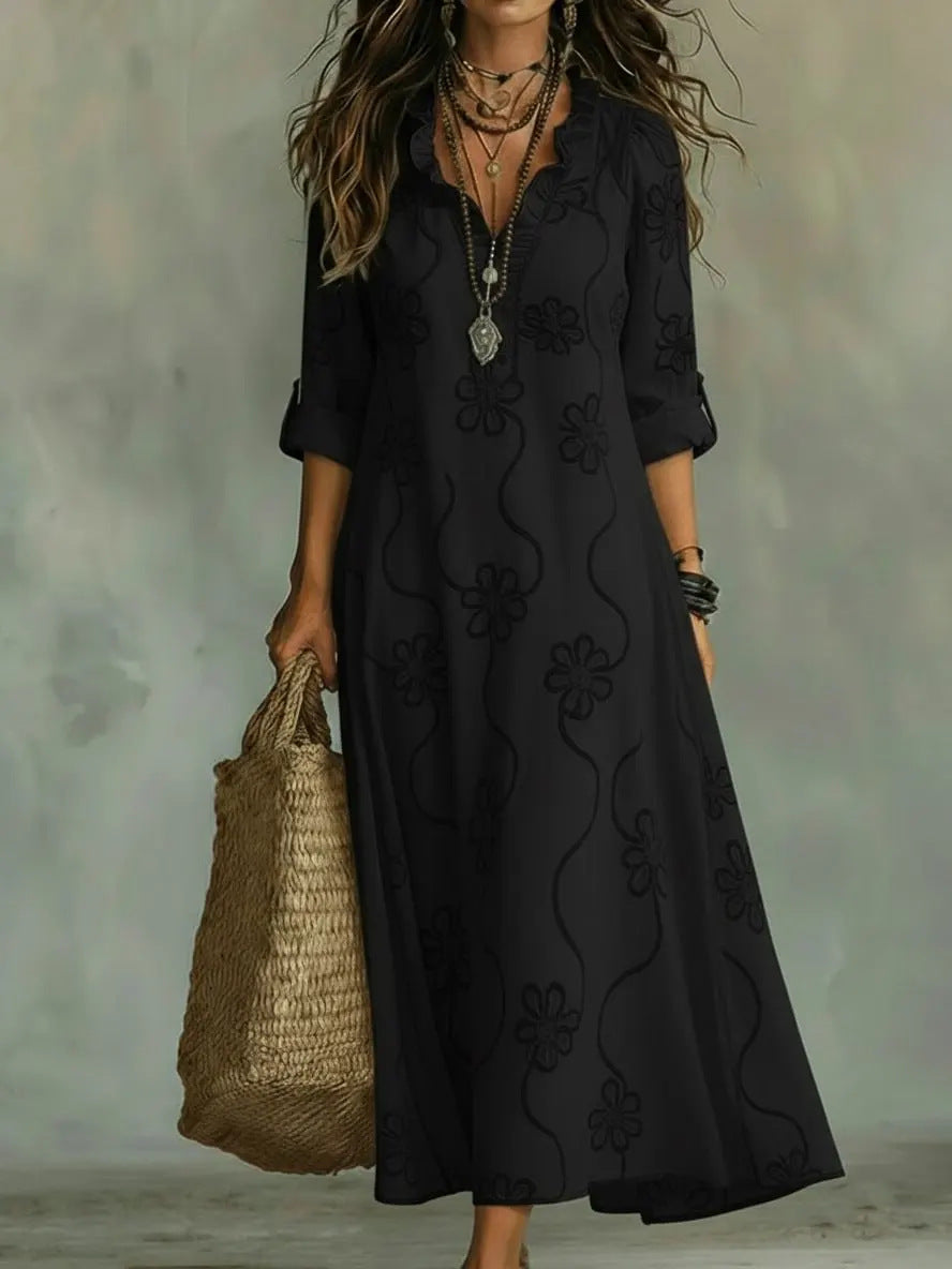 Woman wearing a black dress with floral embroidery, holding a woven bag against a neutral background