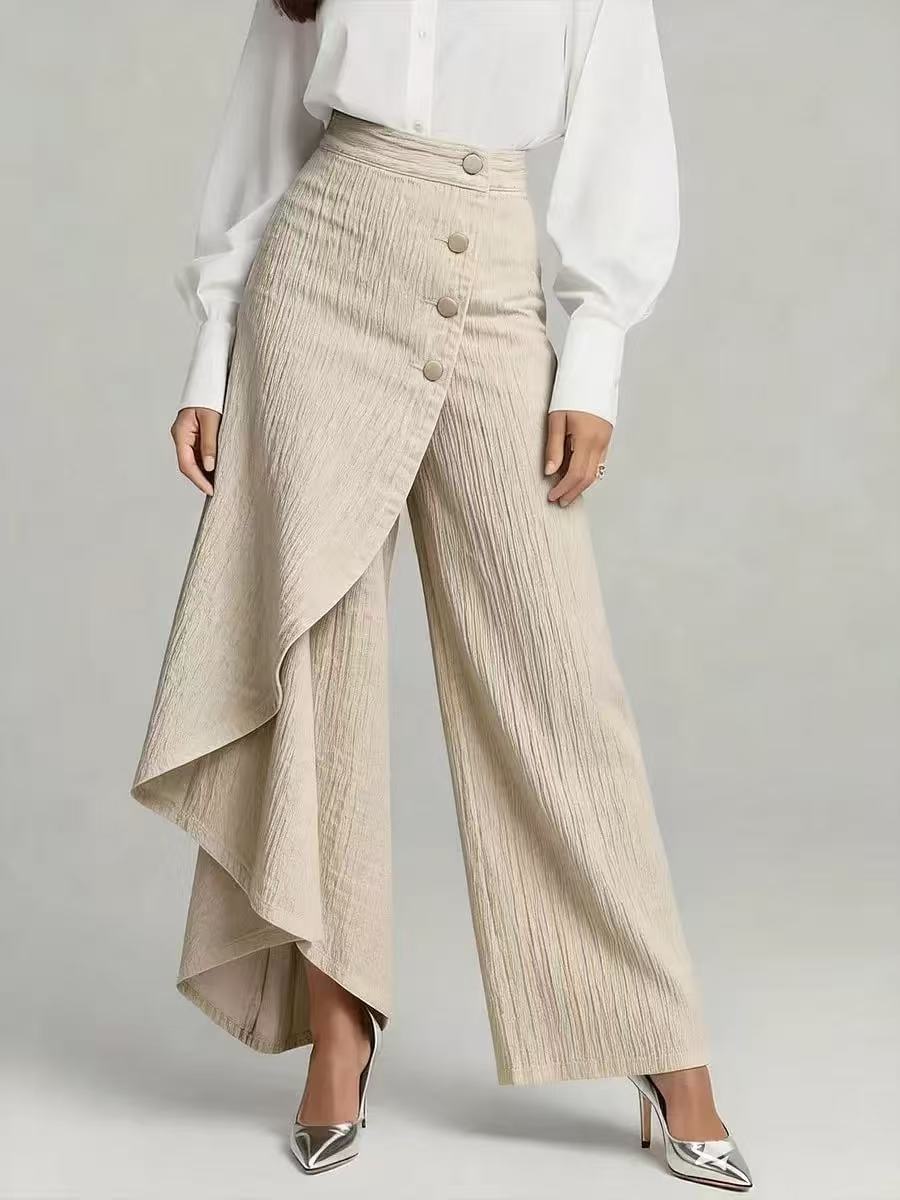 Person wearing a white blouse and beige pleated pants with a button detail on a gray background