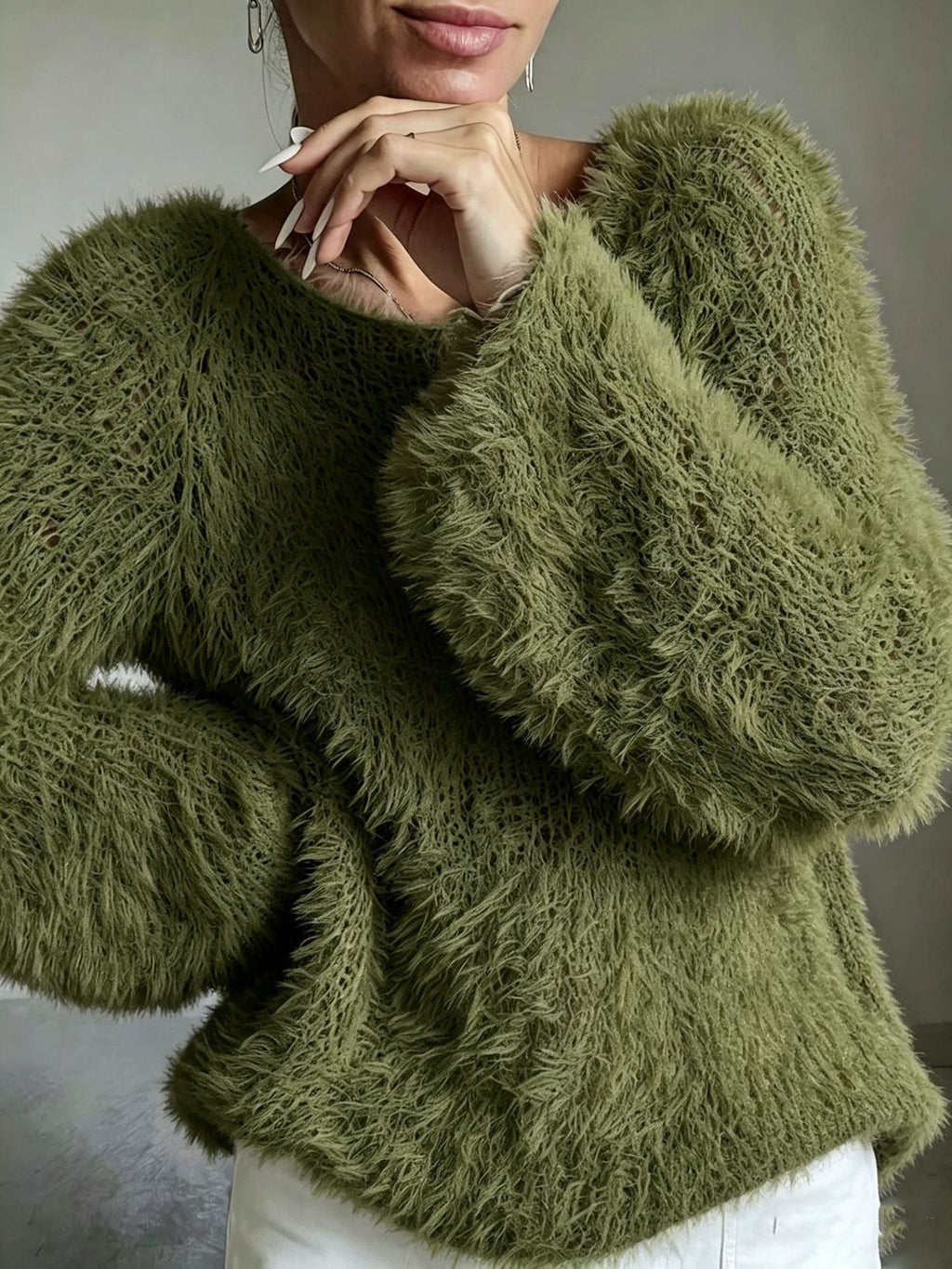A close-up of a woman wearing a fuzzy, textured sage green sweater with voluminous long sleeves, paired with white pants.