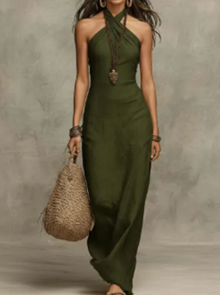 Woman wearing a green halter neck dress holding a woven bag against a gray background