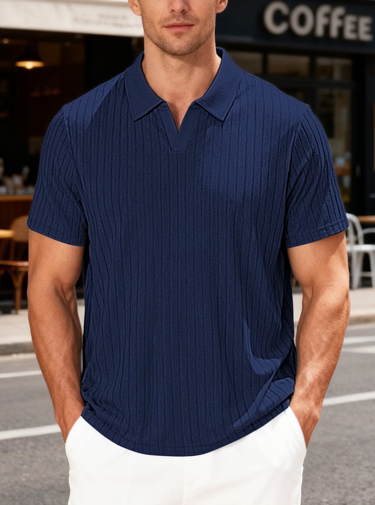 Man wearing a blue ribbed polo shirt standing outdoors with a coffee shop in the background.