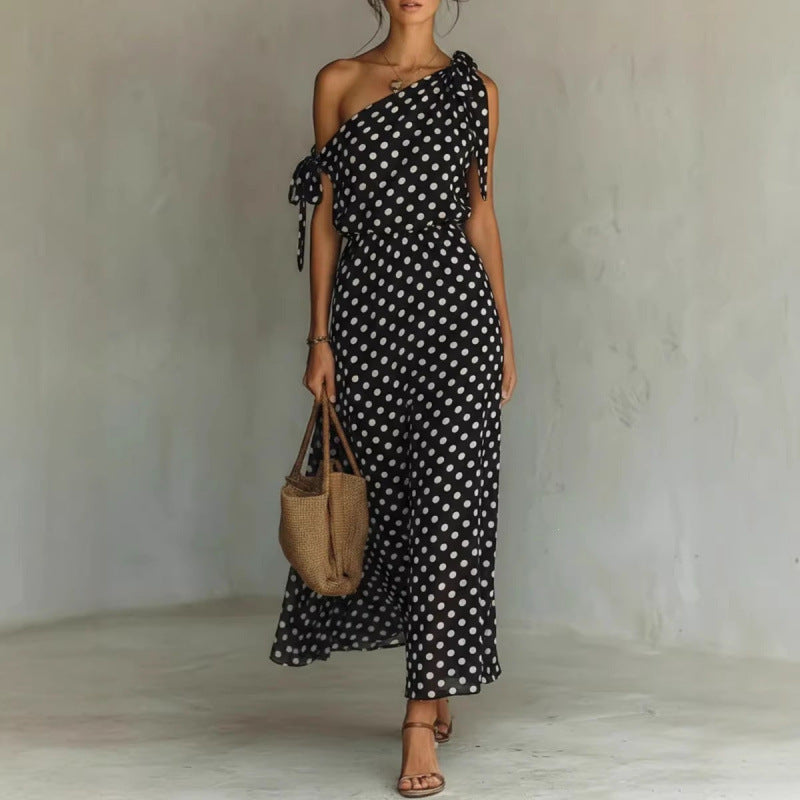 Woman wearing a black polka dot dress holding a woven bag against a plain background