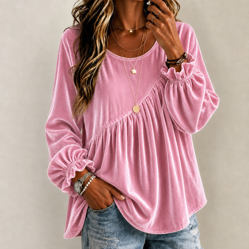 A woman wearing a pink long-sleeve velvet top with ruffled cuffs and a gathered waist, paired with blue jeans, against a neutral beige background.