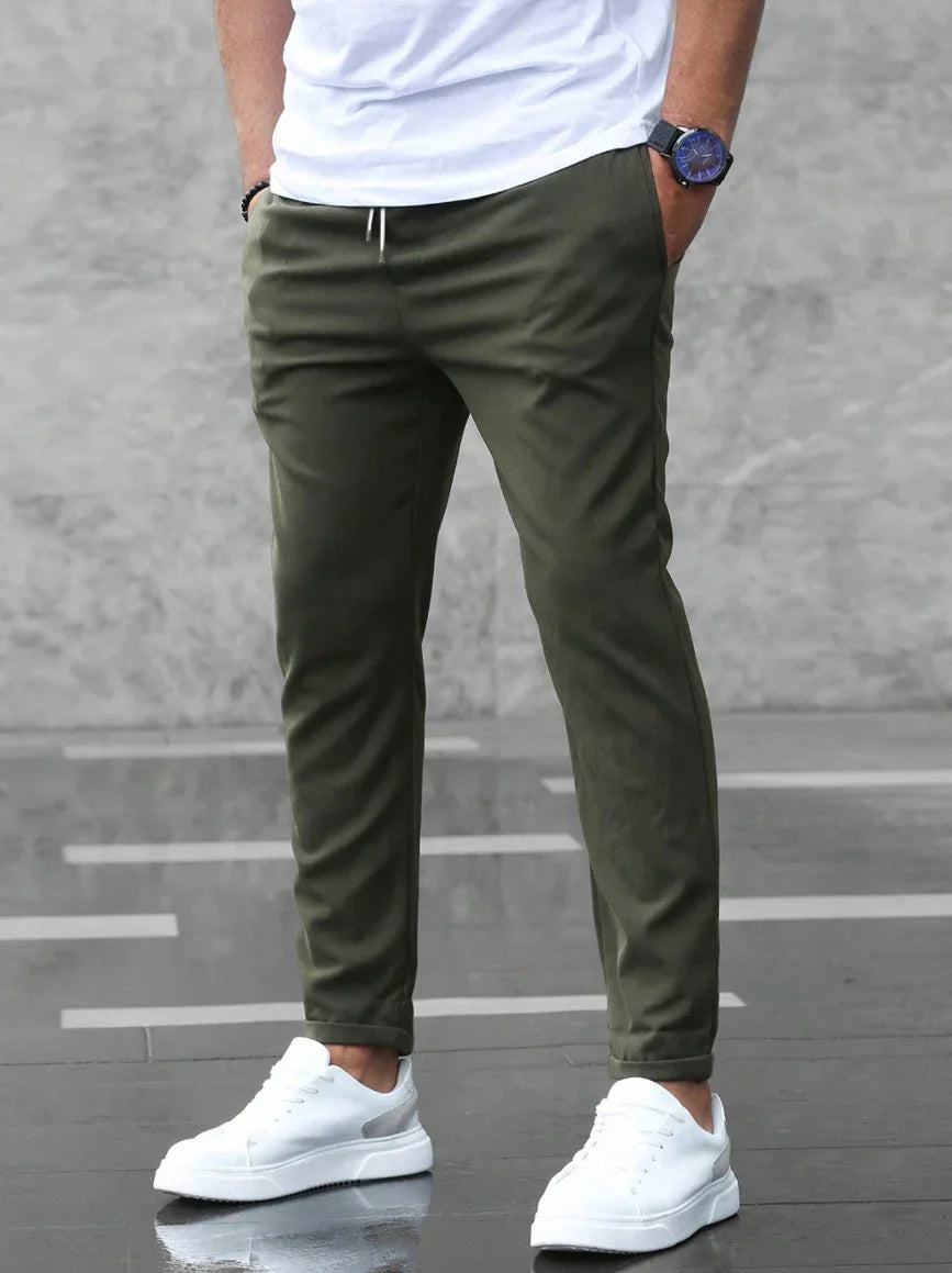 Person wearing olive green pants and white sneakers on a gray pavement.