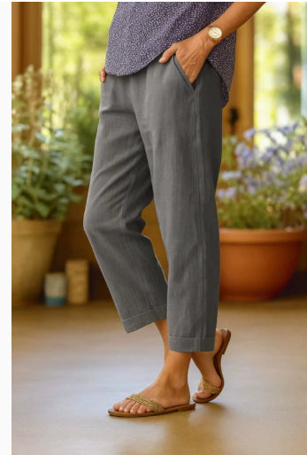 Person wearing gray pants standing indoors with plants in the background