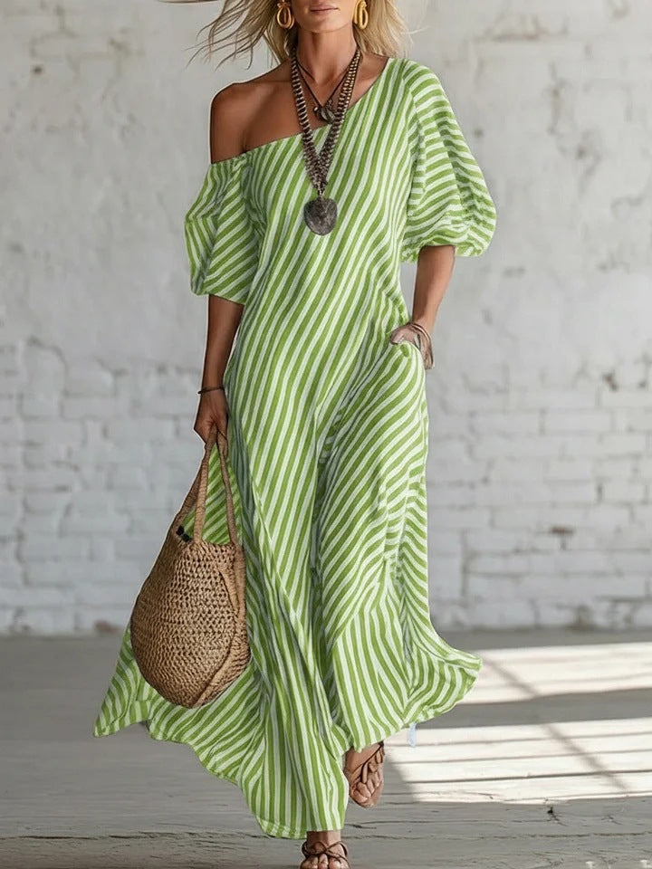 Woman wearing a green and white striped dress holding a woven bag against a white brick wall.