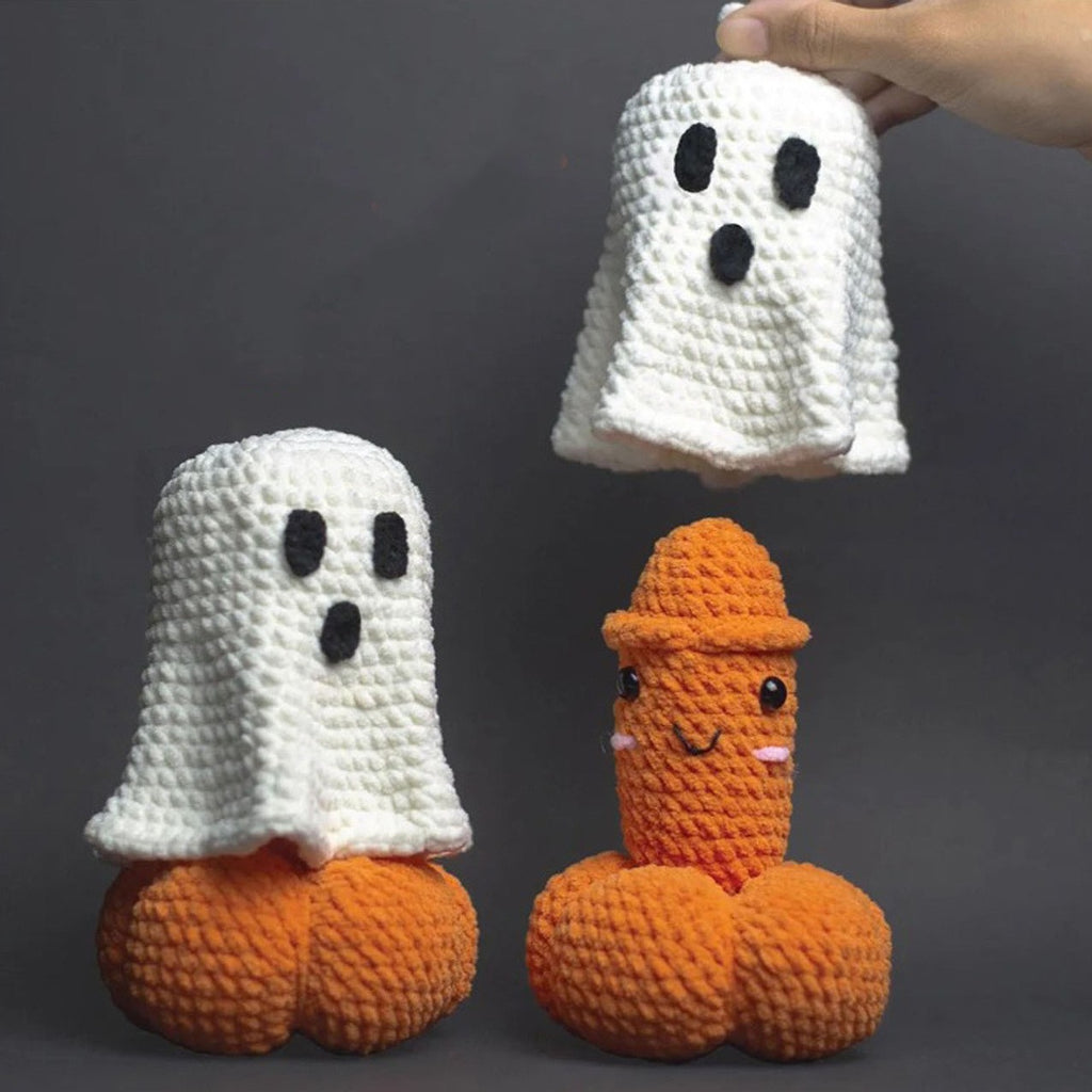 Three crocheted ghost-shaped accessories displayed against a dark gray background: two orange-and-white pairs on the floor and one white pair held by a hand at the top right. The items appear to be novelty socks or sock covers with black embroidered eyes and mouth details.