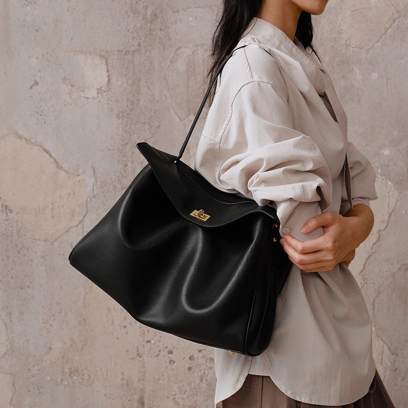 Person holding a black leather handbag against a textured wall.