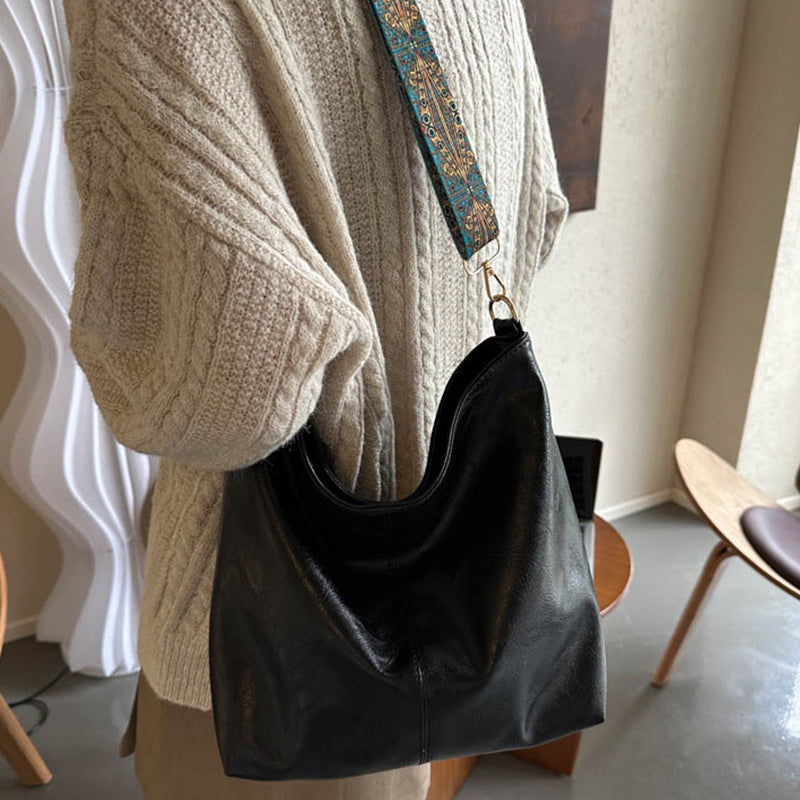 Person wearing a beige sweater holding a black leather handbag with a patterned strap.