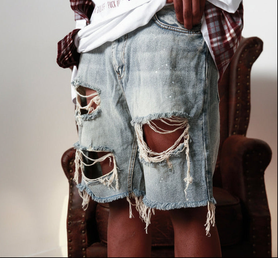 Person wearing ripped denim shorts sitting on a chair with a neutral background