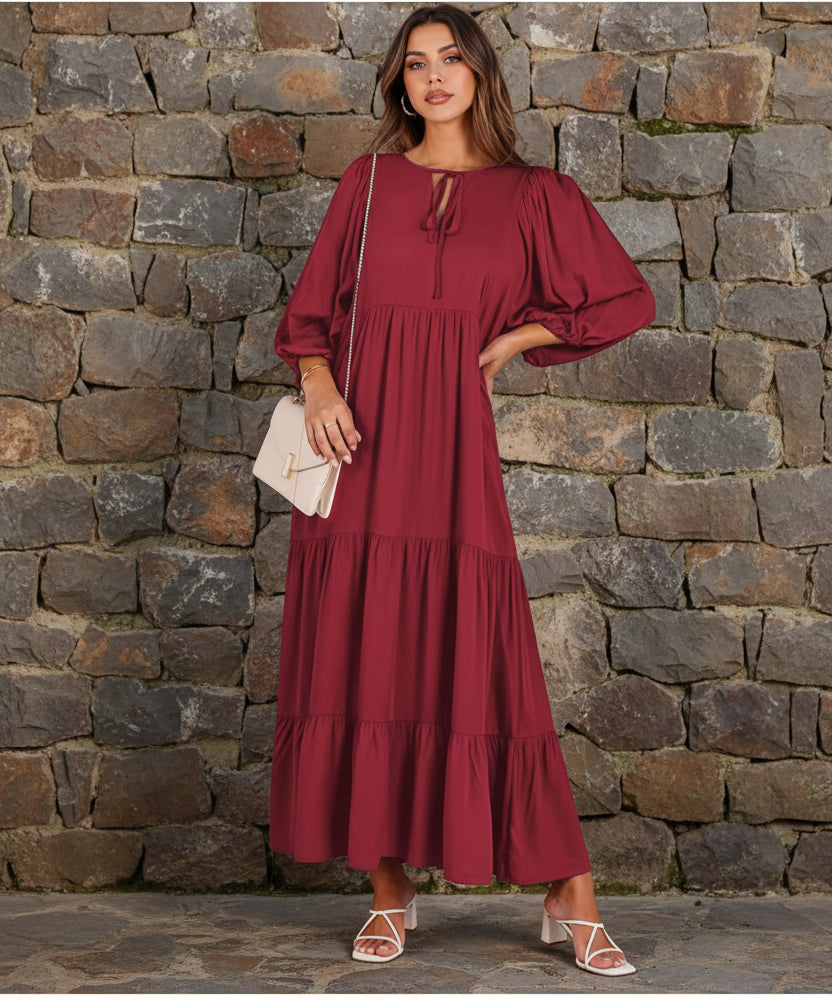 Red dress with long sleeves and tiered skirt standing against a stone wall.