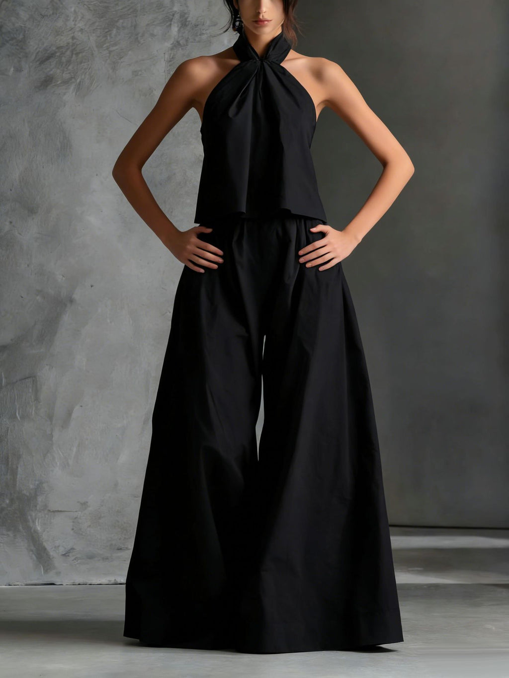 Black jumpsuit worn by a model against a gray concrete background