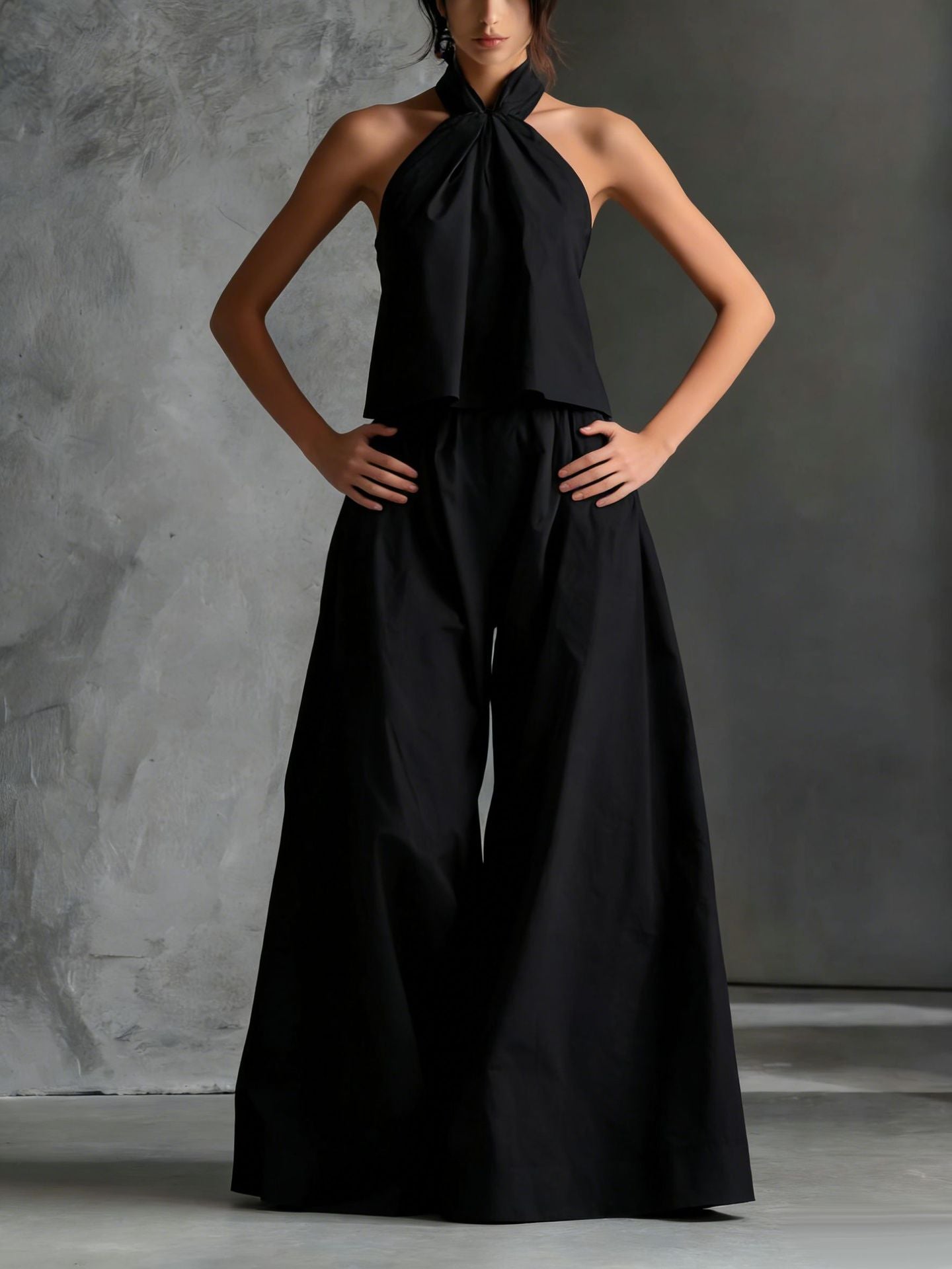 Black jumpsuit worn by a model against a gray concrete background