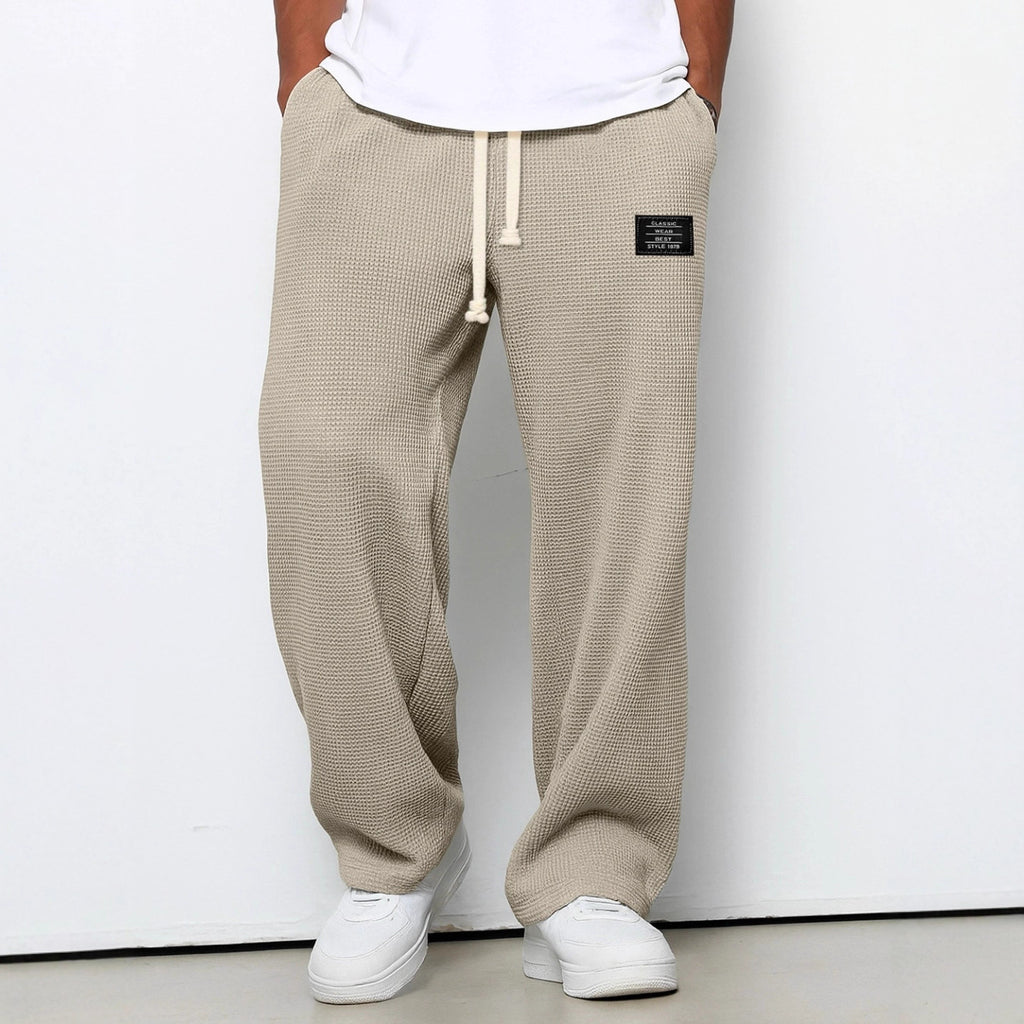Beige waffle-textured pants with a brand logo worn by a person on a white background