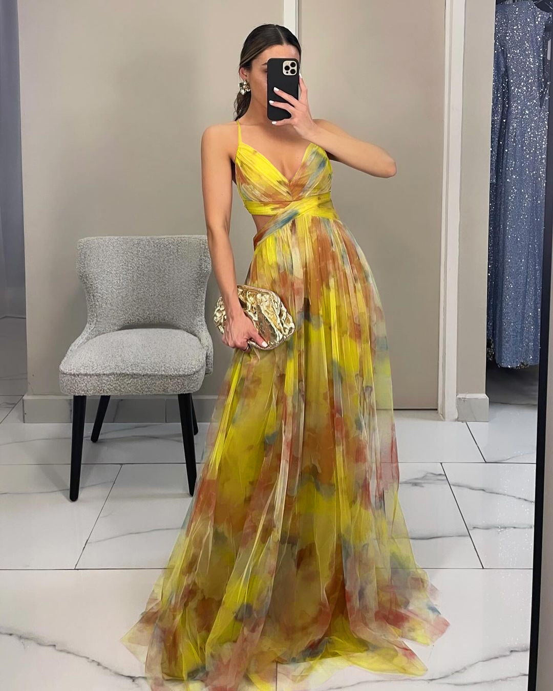 Woman in a yellow floral dress taking a mirror selfie in a store.
