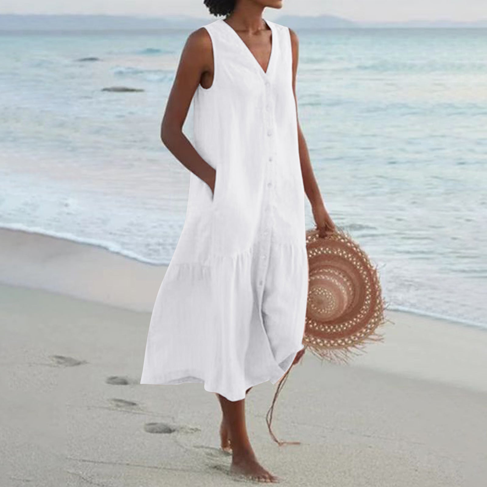 Woman in a white dress holding a straw hat on a beach
