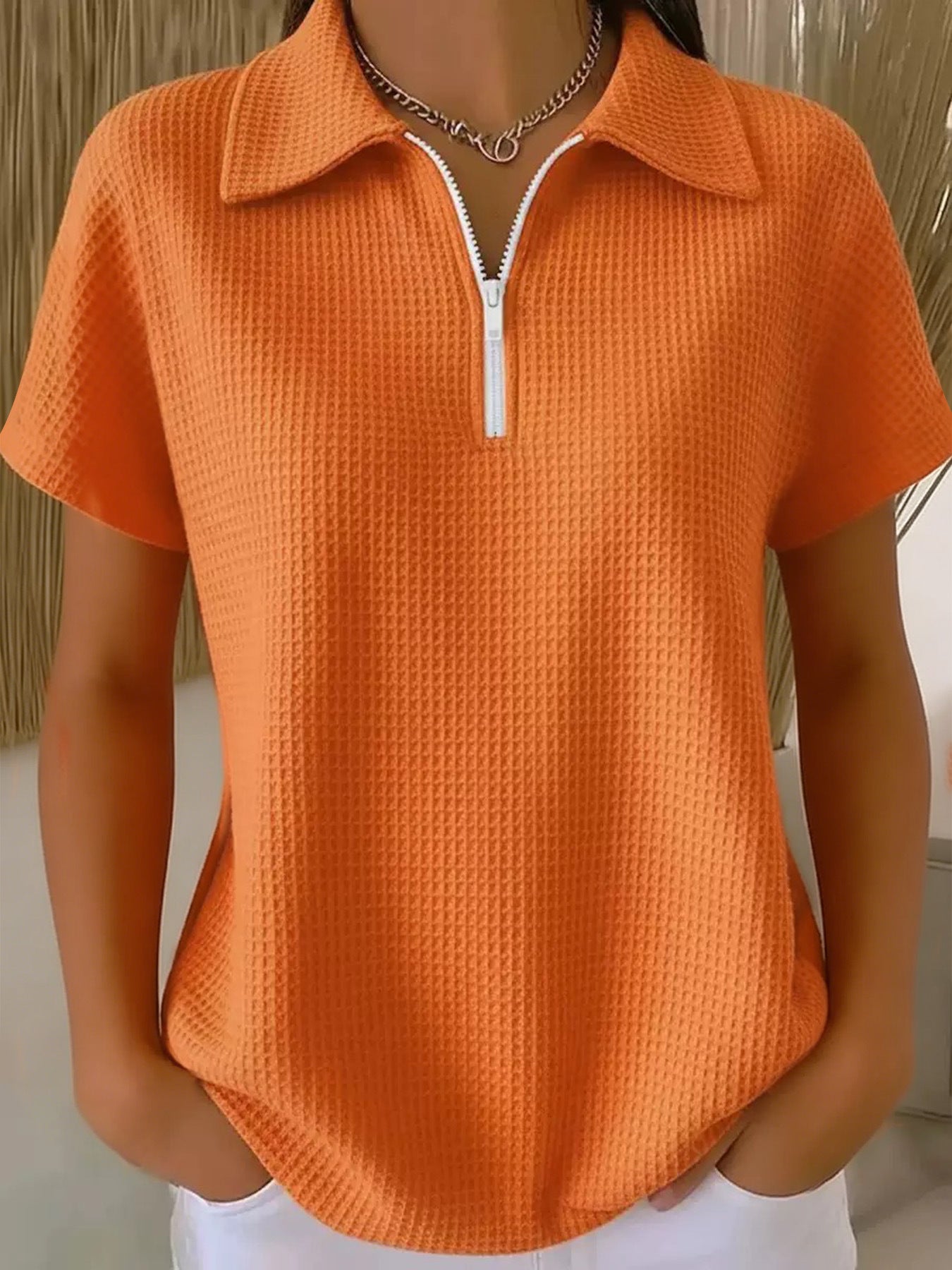 Orange textured short-sleeve shirt with a zipper on a neutral background
