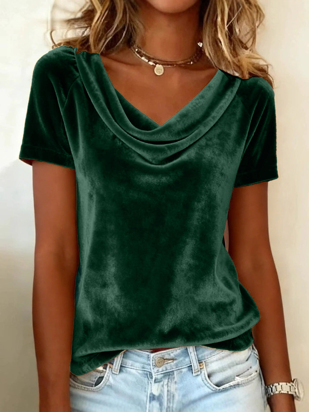 Person wearing a green velvet top and light blue jeans against a neutral background