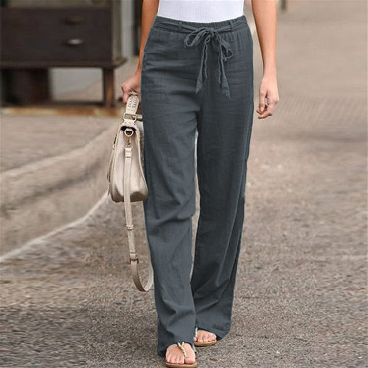 Person wearing gray drawstring pants holding a beige handbag on a street.