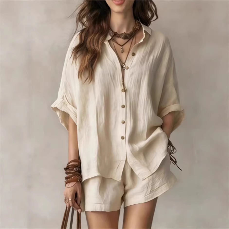 Woman wearing a beige shirt and shorts set with layered necklaces against a neutral background