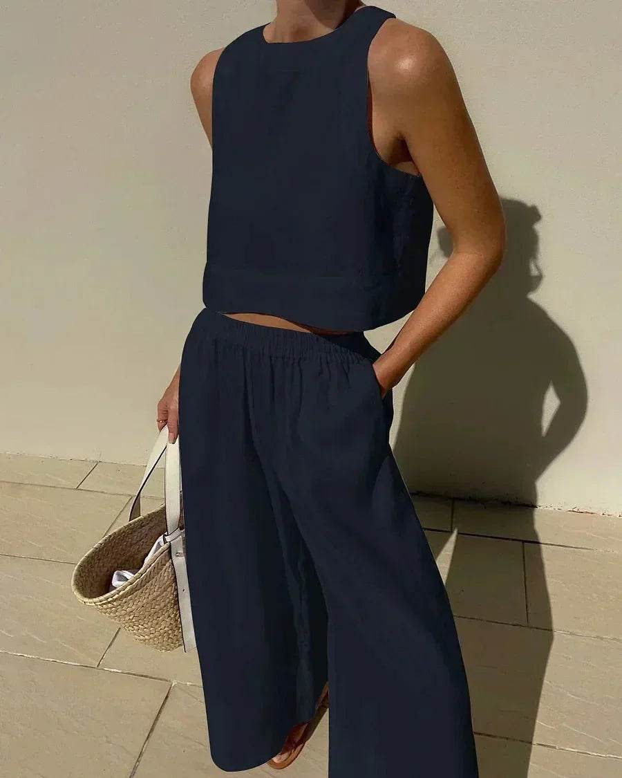 Woman wearing a sleeveless black crop top and wide-leg pants set, holding a straw handbag