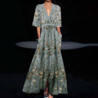 Woman wearing a long, light green dress with floral embroidery on a dark background