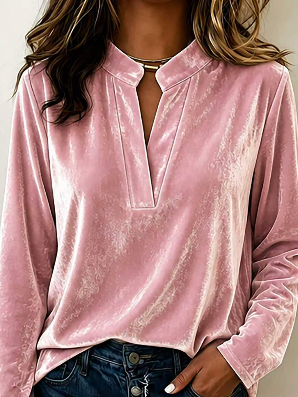A woman wearing a long-sleeve pink velvet top with a split V-neckline and dark blue jeans, shown from the shoulders to the hips against a plain light background.