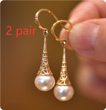 Gold and pearl earrings held by a hand with a brown background