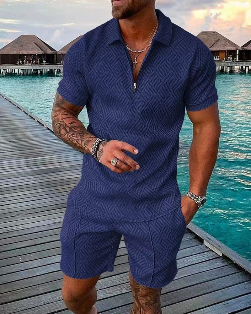 Man wearing a blue textured outfit standing on a wooden dock by the water.