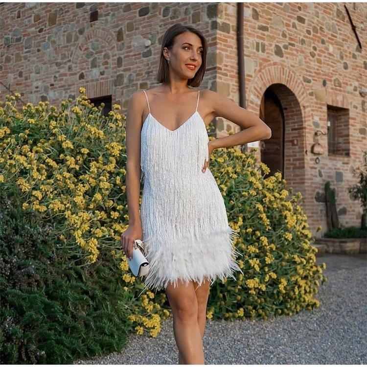 Woman in a white fringe dress standing in front of a stone building with yellow flowers.