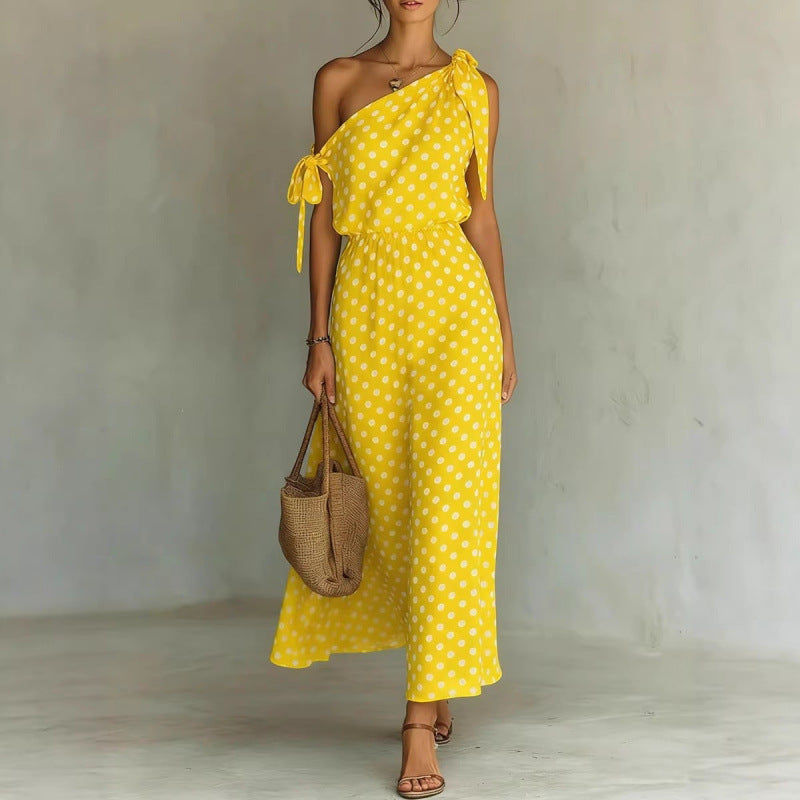 Woman wearing a yellow polka dot dress holding a woven bag against a plain background