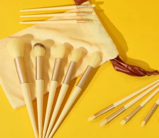 Makeup brush set with wooden handles on yellow background, includes pouch and beauty tools