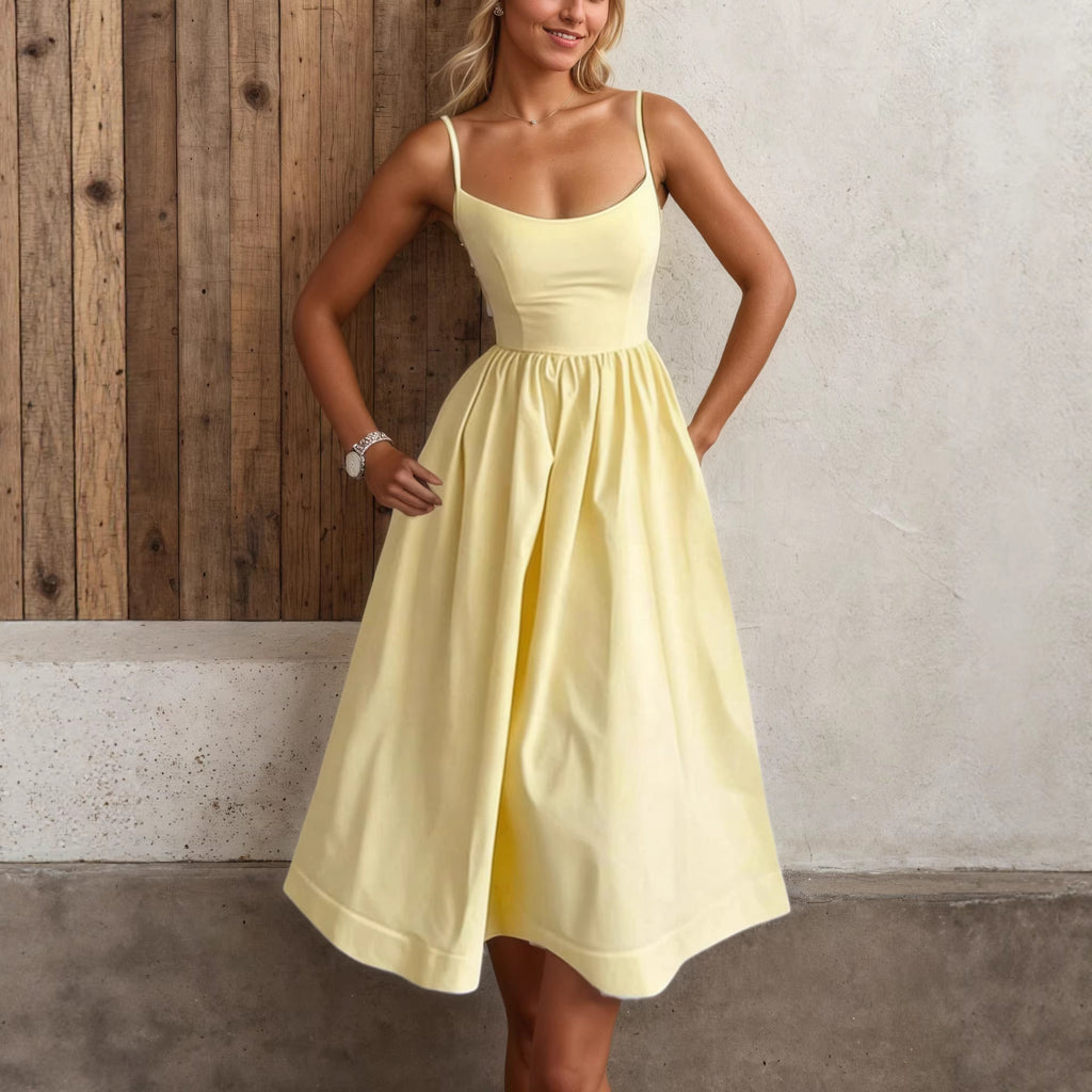 Woman wearing a yellow dress standing against a wooden and concrete wall.