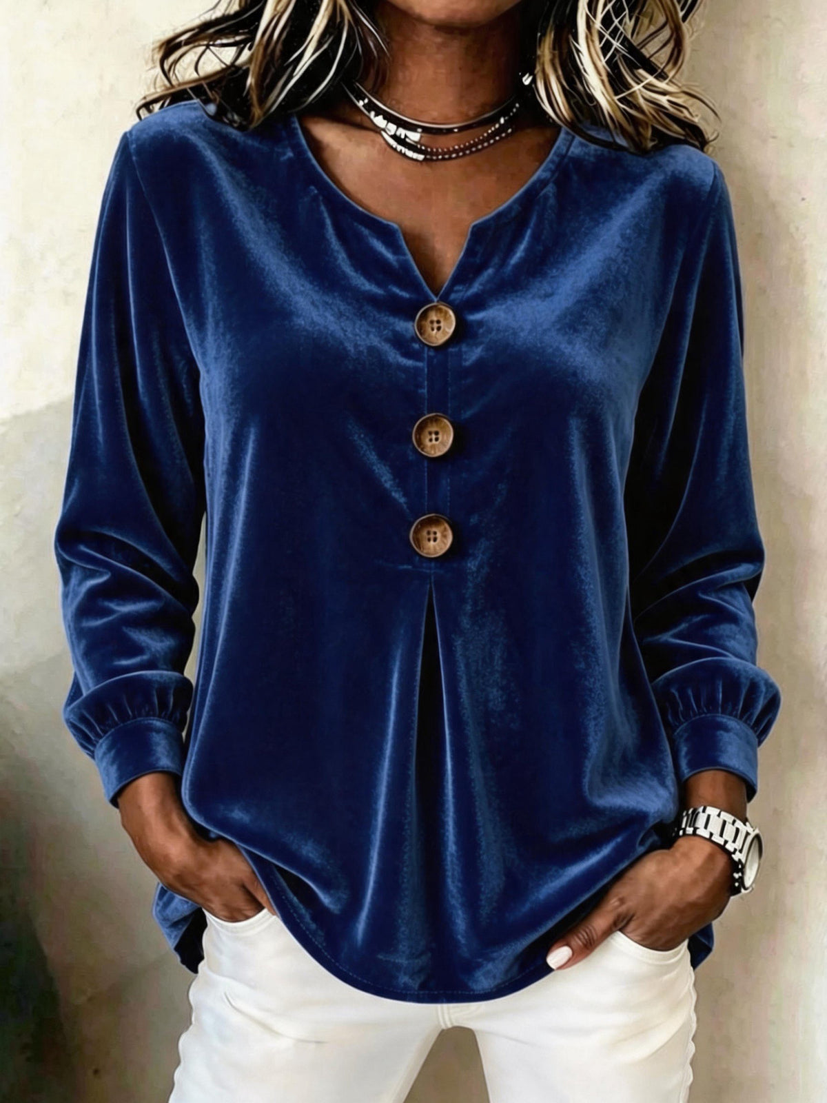 Person wearing a blue velvet blouse with buttons, standing against a neutral background