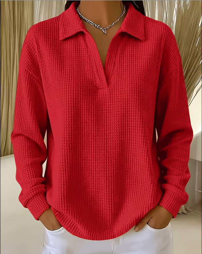 A woman wearing a bright red waffle-knit long-sleeve collared shirt with a split V-neck, paired with white pants and a silver necklace.