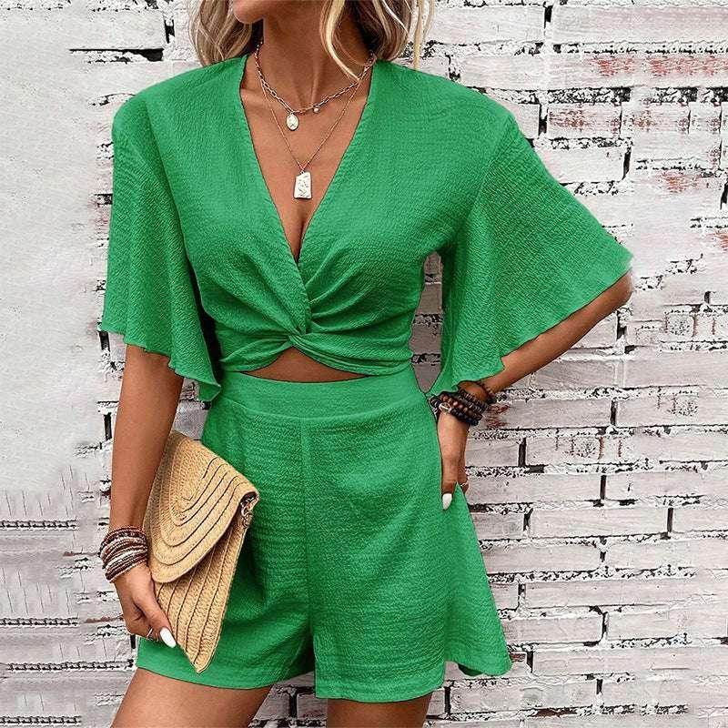 Woman wearing a trendy green short set outfit from ZA-Zola, accessorized with jewelry and a clutch, standing against a white brick wall.