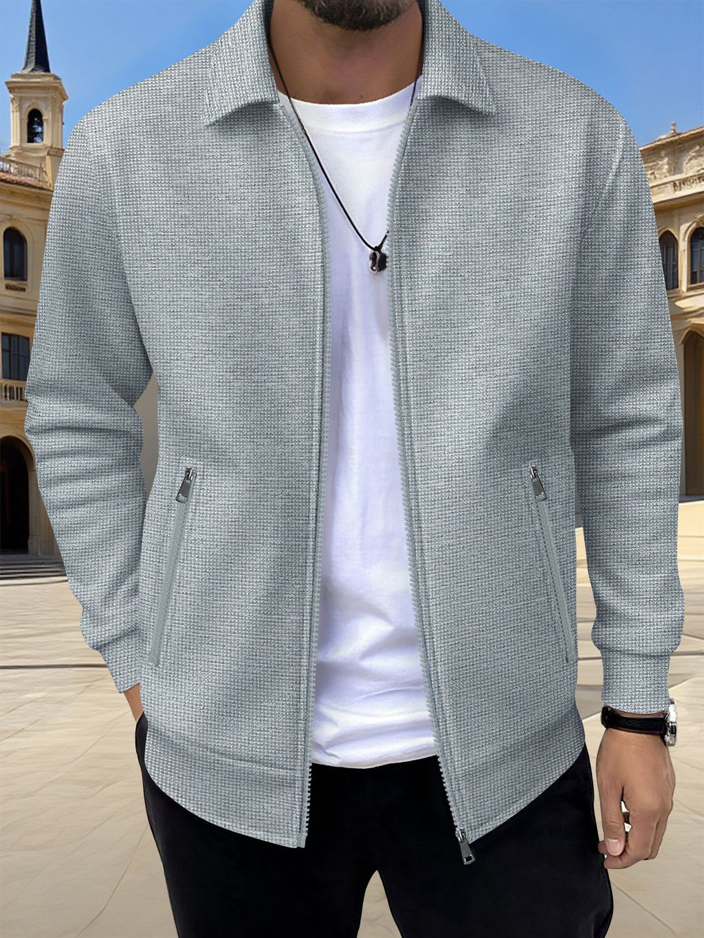 Man wearing a light gray textured jacket over a white shirt with a blurred architectural background