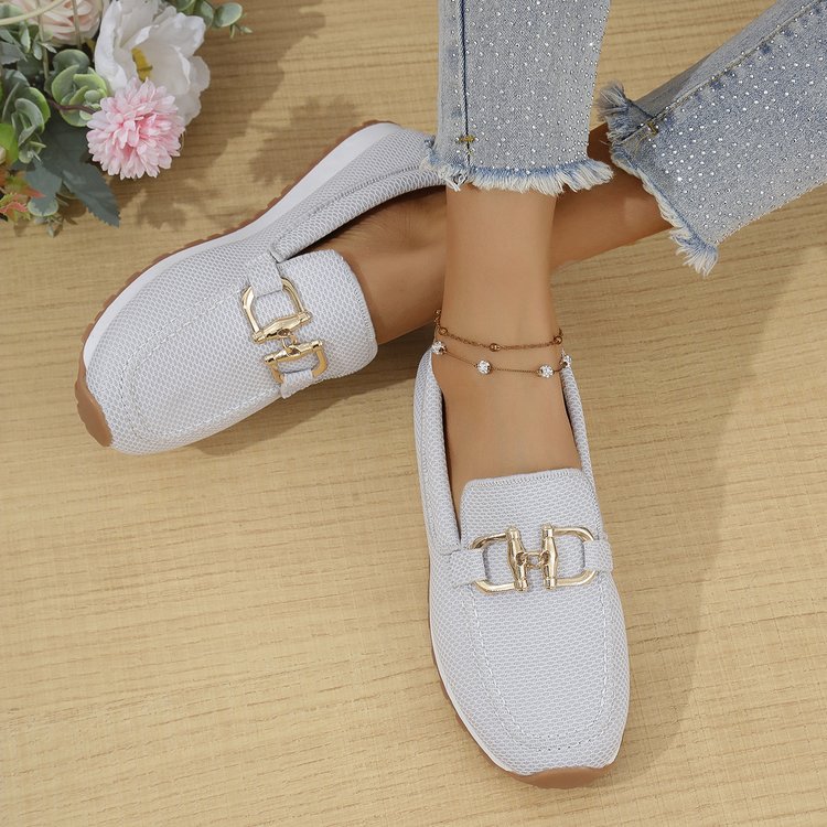 White loafers with gold buckles worn by a person on a wooden floor.
