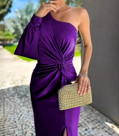 Woman in a purple one-shoulder dress holding a gold clutch outdoors.