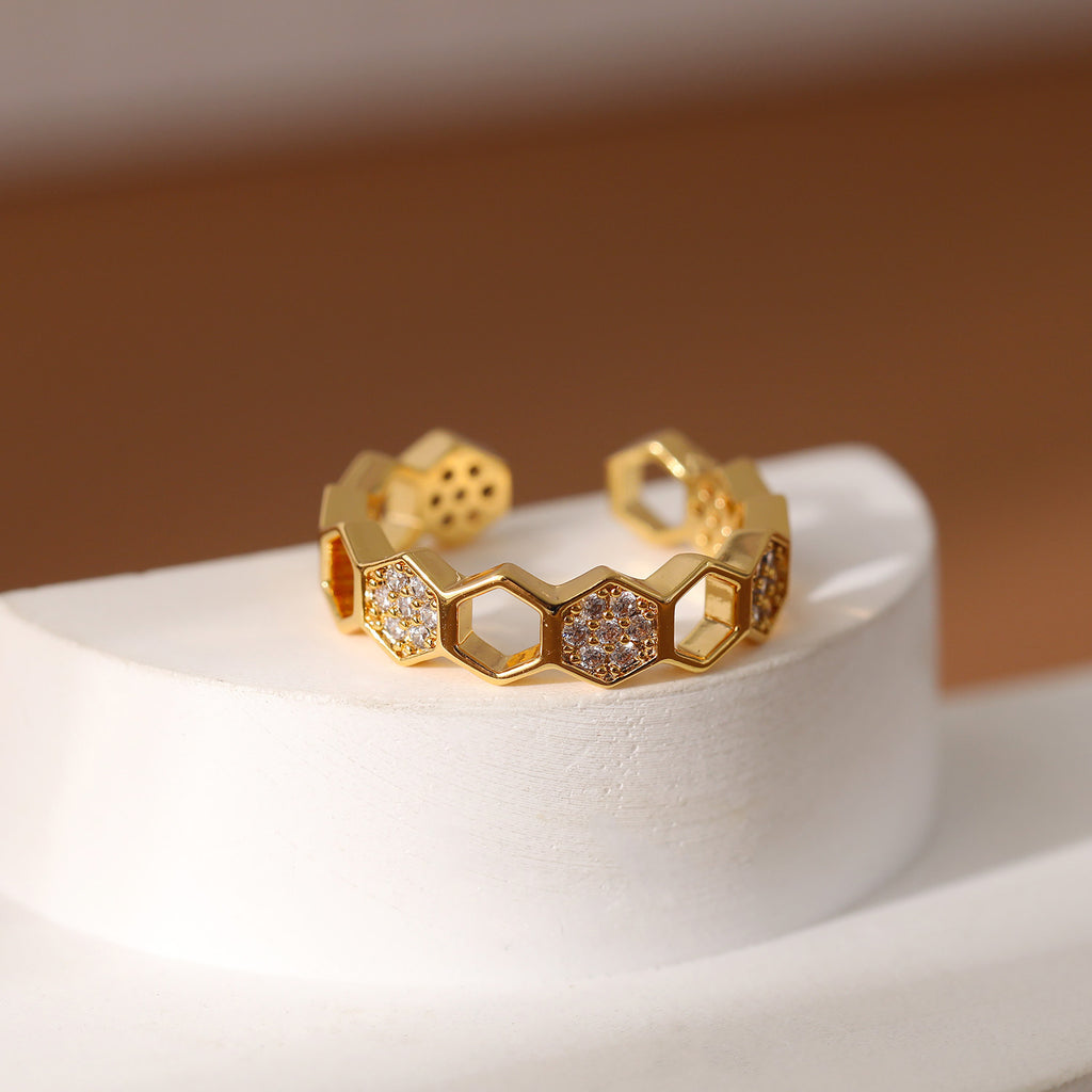 Gold ring with honeycomb design and embedded stones on a white stand with a brown background