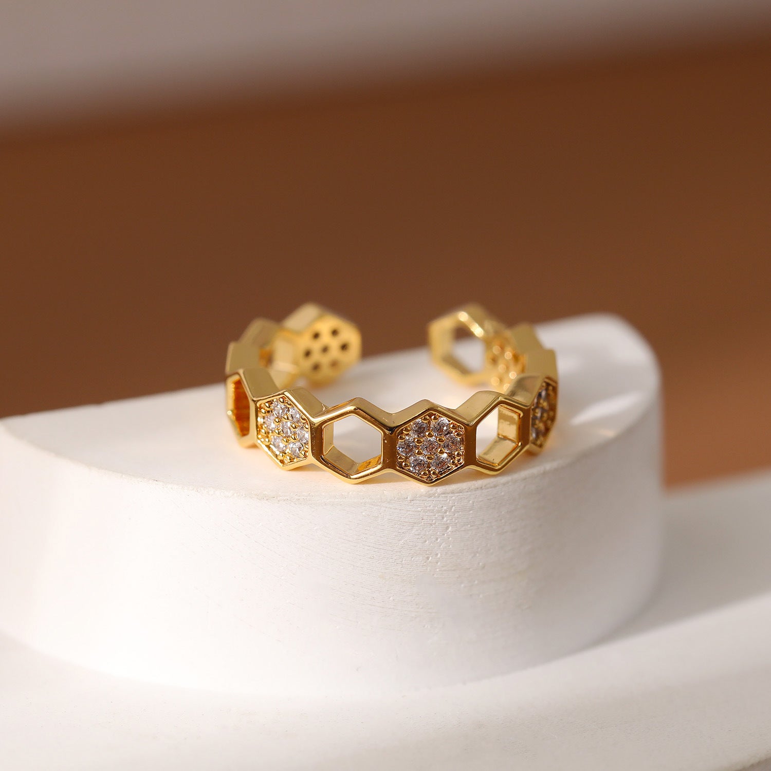 Gold ring with honeycomb design and embedded stones on a white stand with a brown background