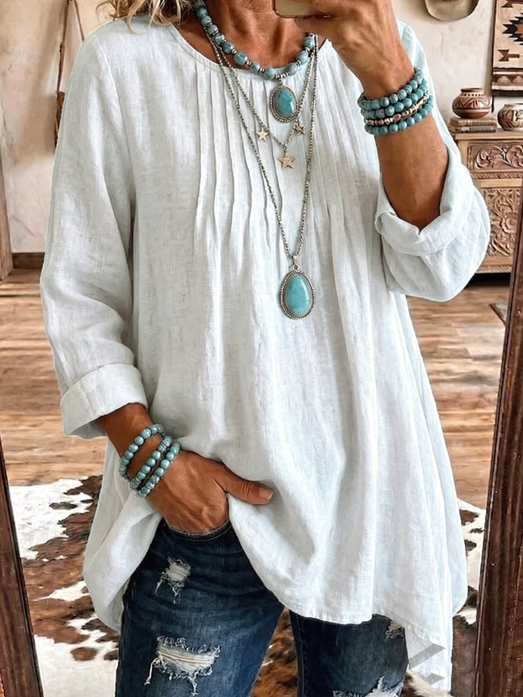 A woman takes a mirror selfie wearing a loose white linen-blend tunic top with rolled sleeves, paired with distressed blue jeans and layered turquoise and silver jewelry.