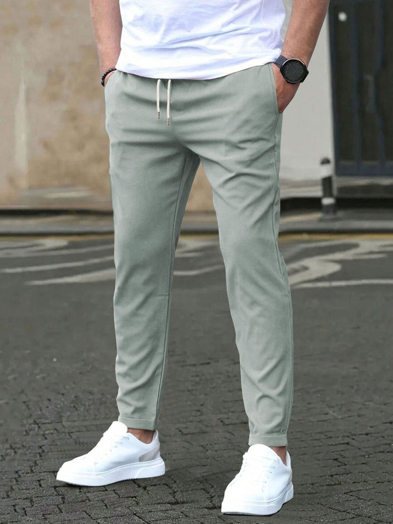 Person wearing light green jogger pants with a white shirt and white sneakers on a street.