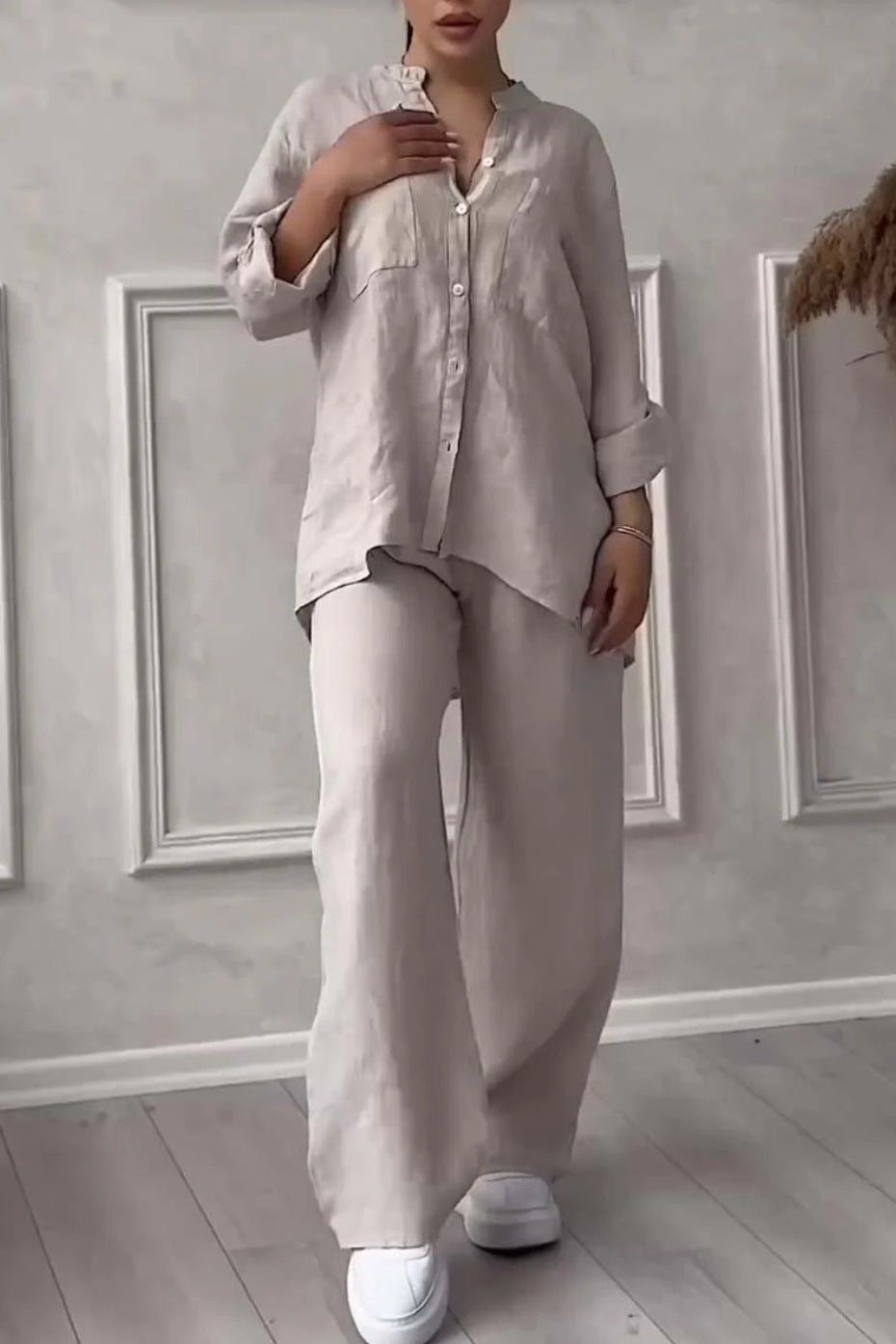 Person wearing a light beige shirt and pants in a minimalistic room.