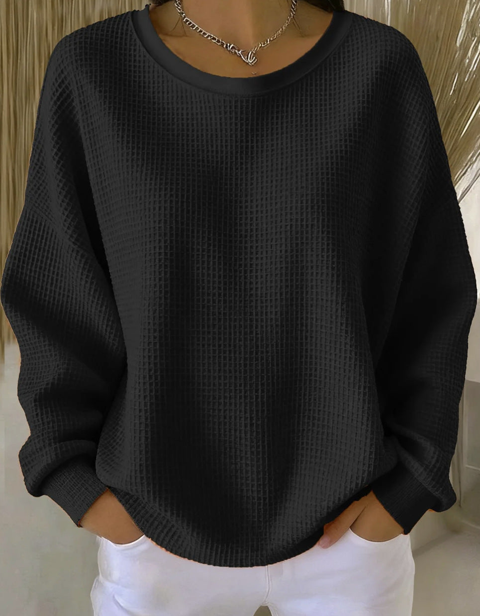 Person wearing a black textured sweater and white pants against a neutral background
