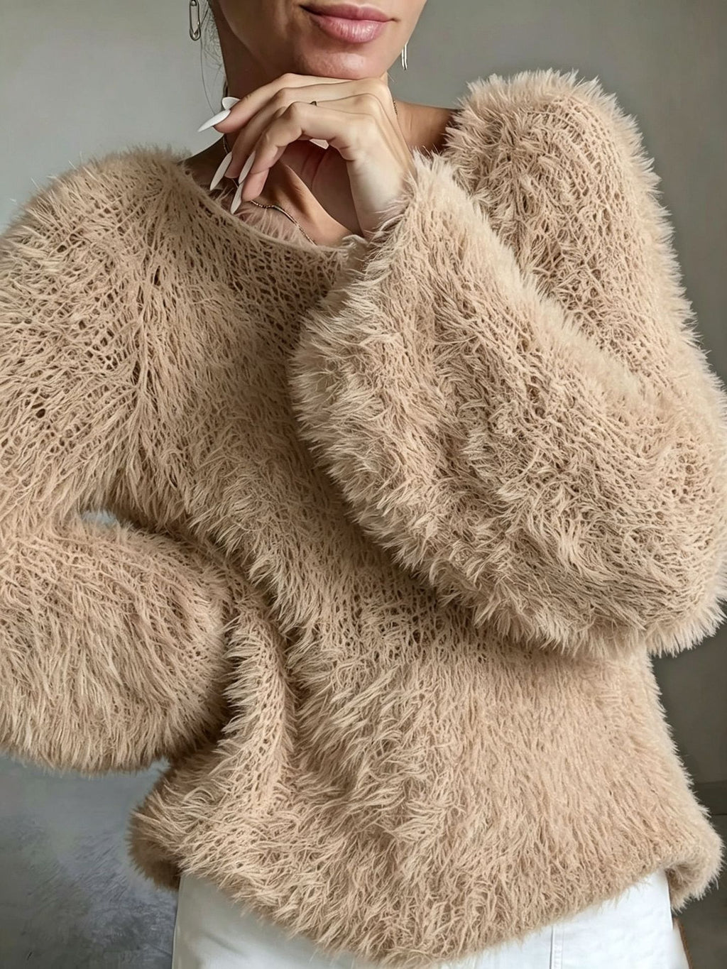 A close-up of a woman wearing a fuzzy, textured knit sweater in a warm beige or light tan color, paired with white pants.