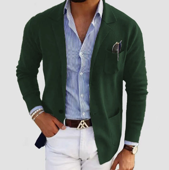 Man wearing a green blazer over a striped shirt with white pants on a light gray background