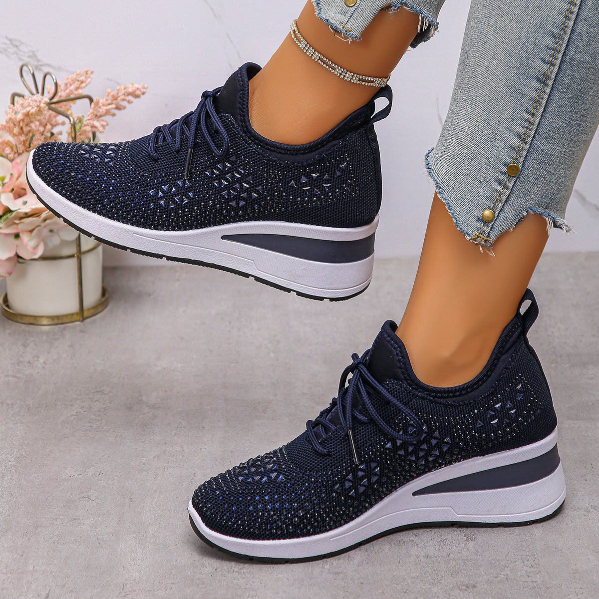 Navy blue athletic shoes with white soles worn by a person on a light gray surface.
