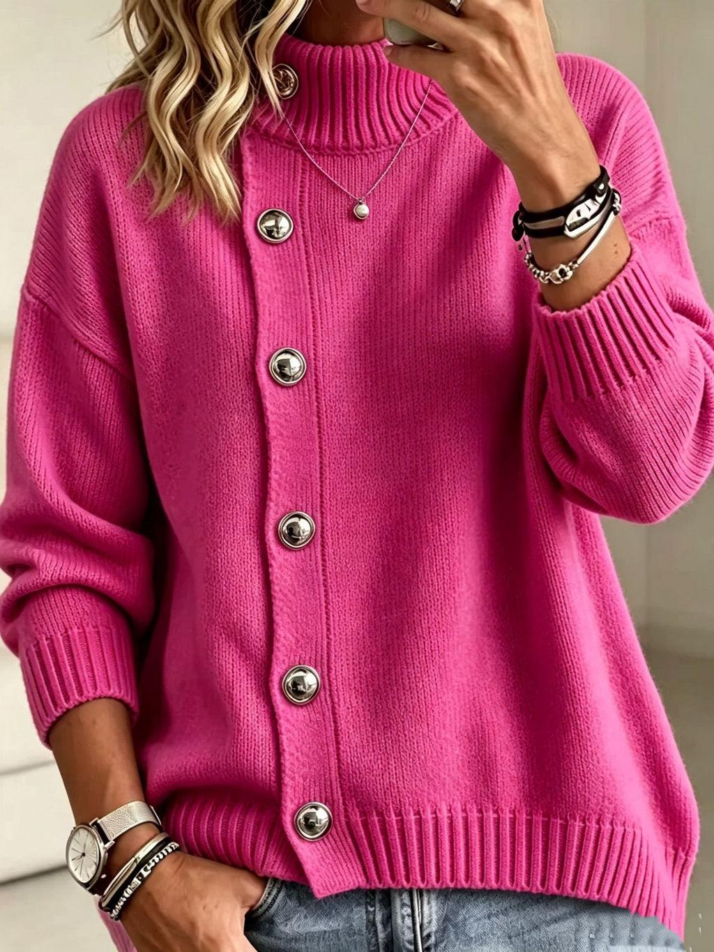 A woman wearing a bright pink knit cardigan sweater with a mock neck, silver-tone buttons, and ribbed cuffs and hem, paired with blue jeans.